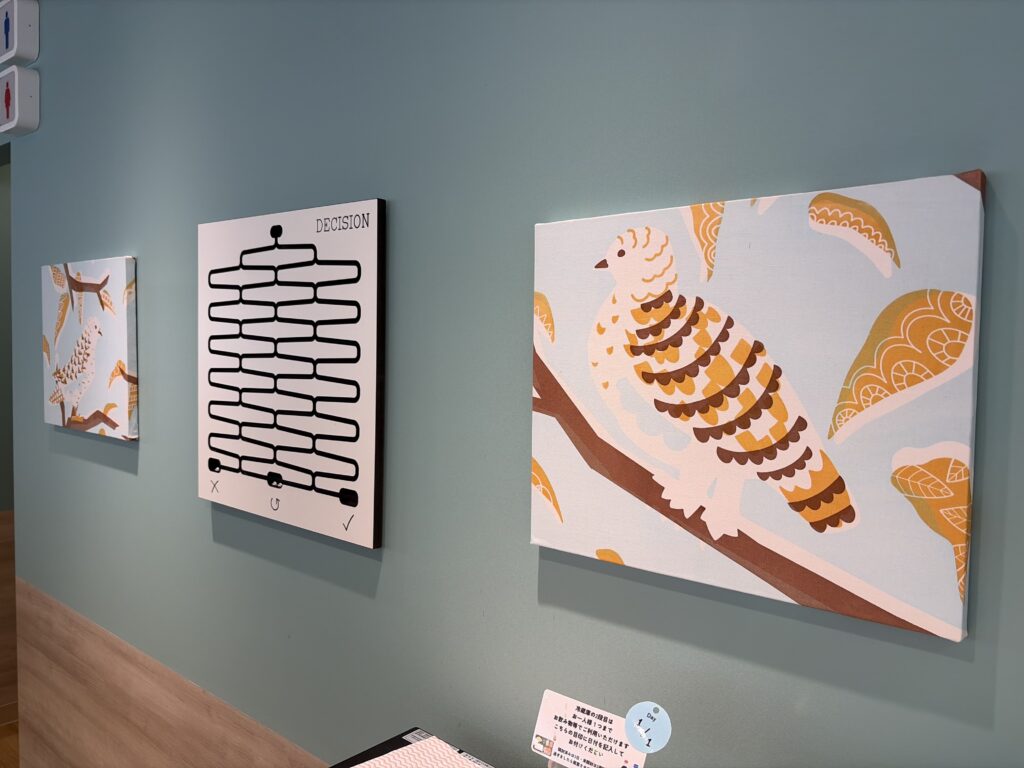 IMG_3724 - Share Nest 仙川 Three artworks on a teal wall: a small orange-and-white bird design on the left, a middle black 'DECISION' diagram, and a large orange fish pattern on the right.