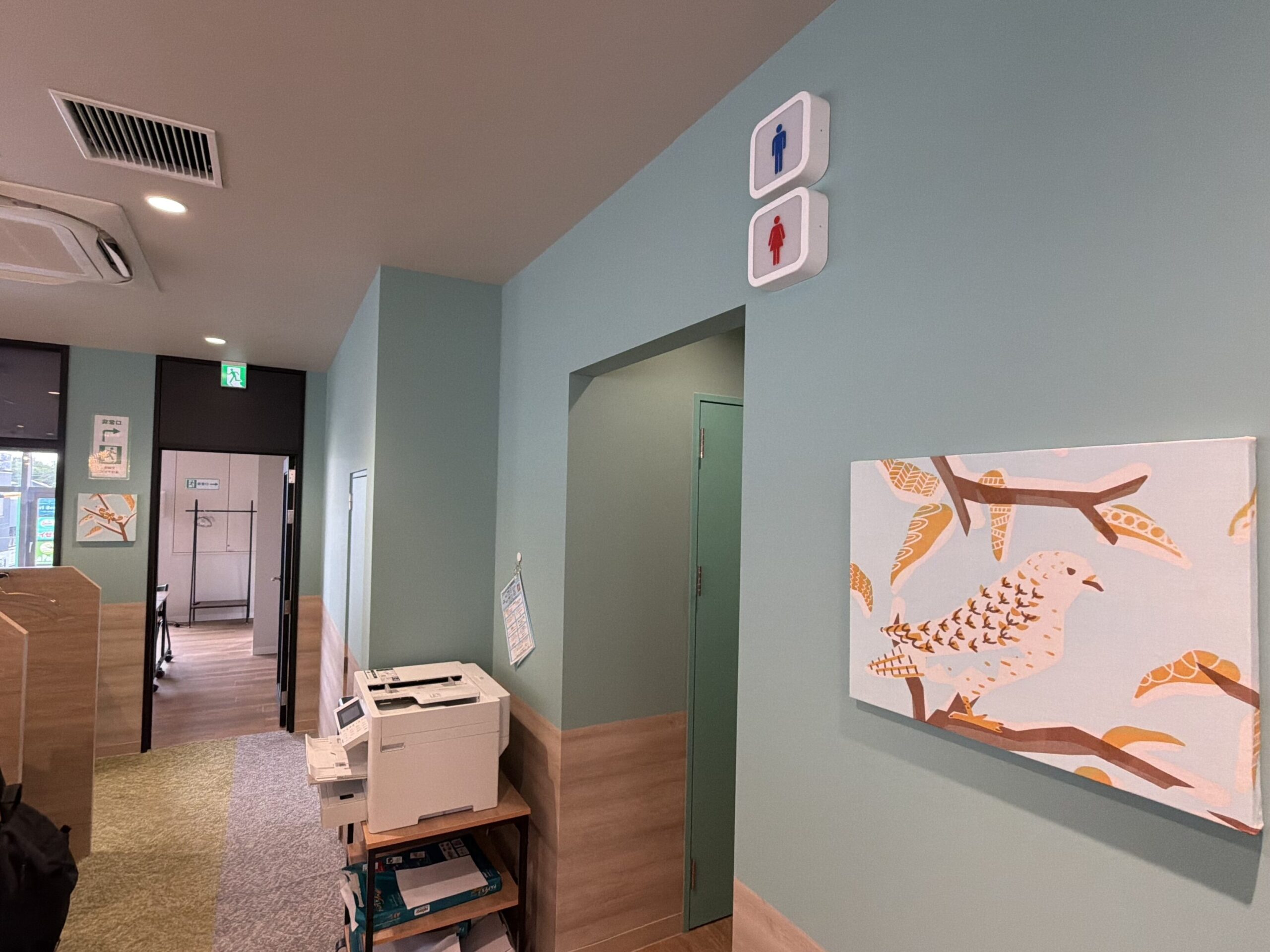 IMG_3726 - Share Nest 仙川 Interior of an office space with teal walls, a printer on a small table, and wall art depicting orange fish with branches on the right side.